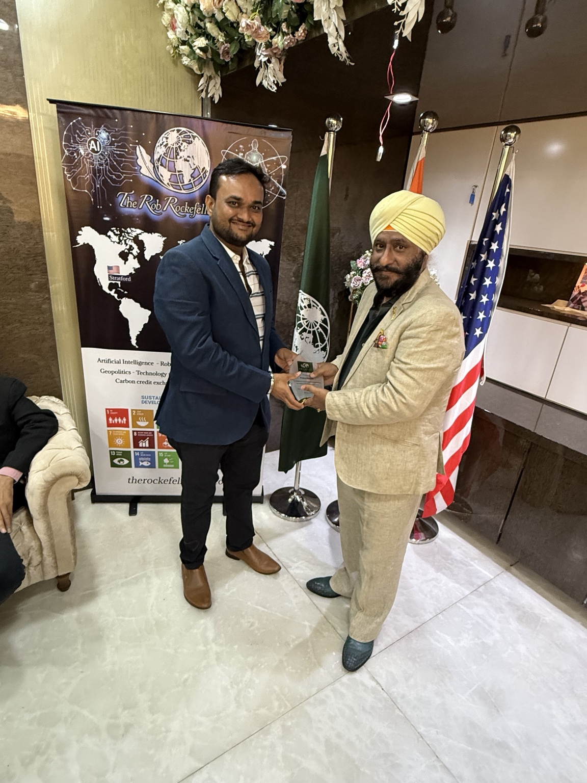 Guests holding a commemorative plaque beside the India Branch flags