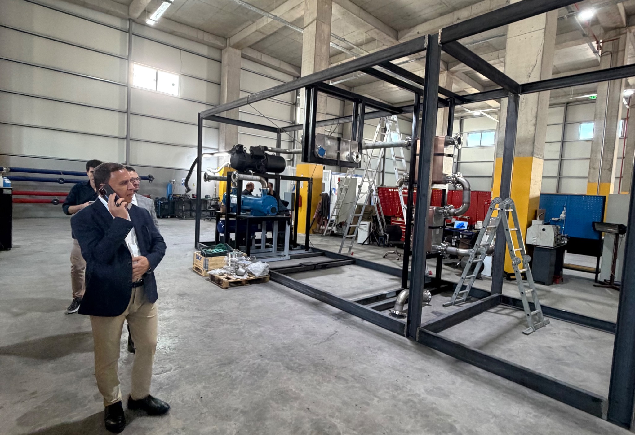 Workshop discussion beside a large equipment frame under assembly.