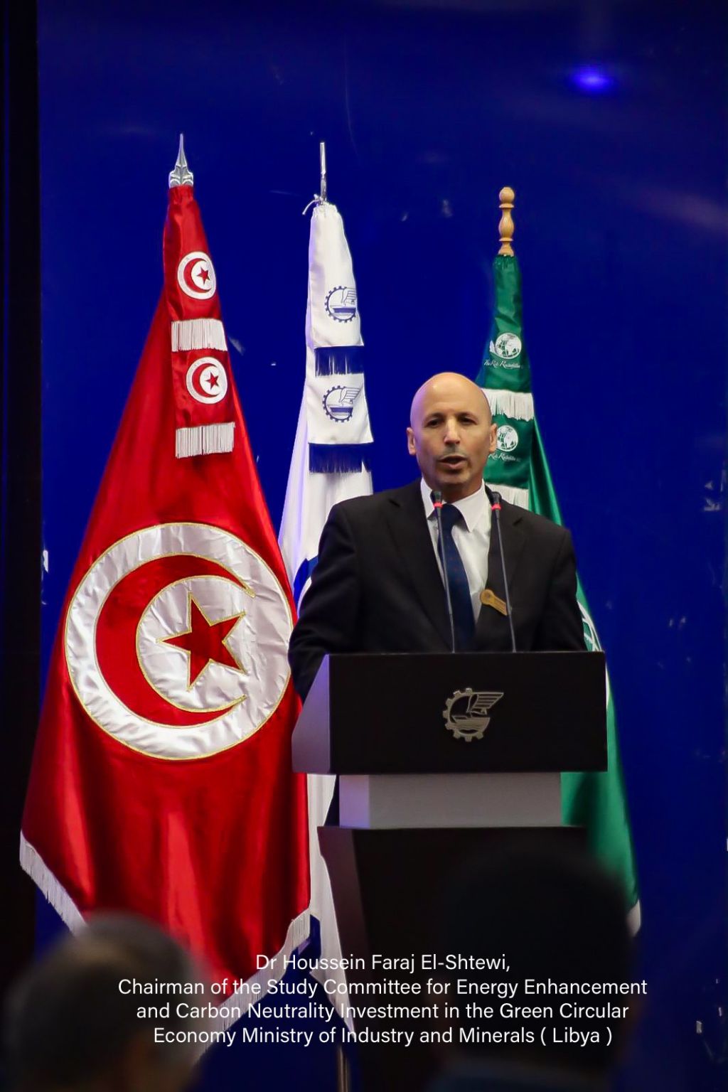 A speaker at the lectern beside the Tunisian, UTICA and RRSC flags