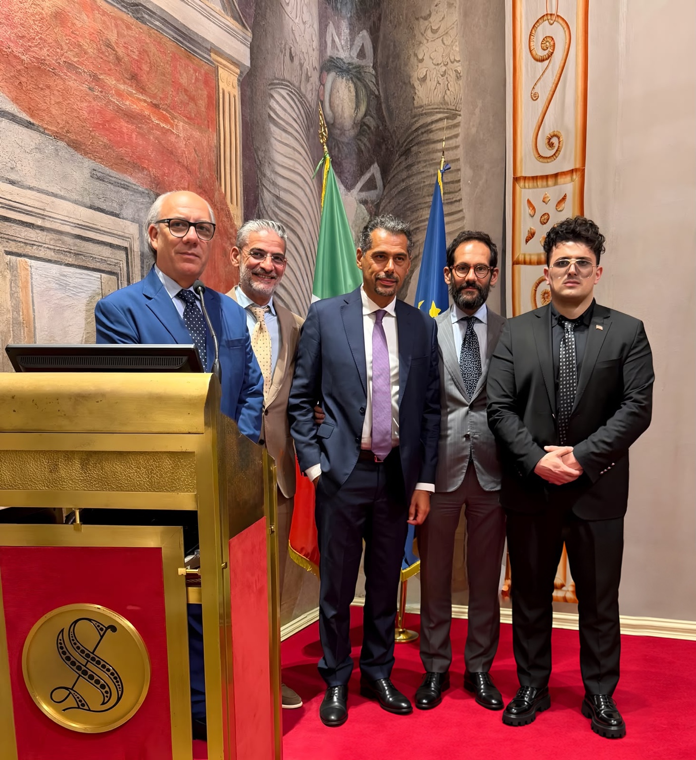 Members of the project delegation beside the Senate lectern and Italian and European flags
