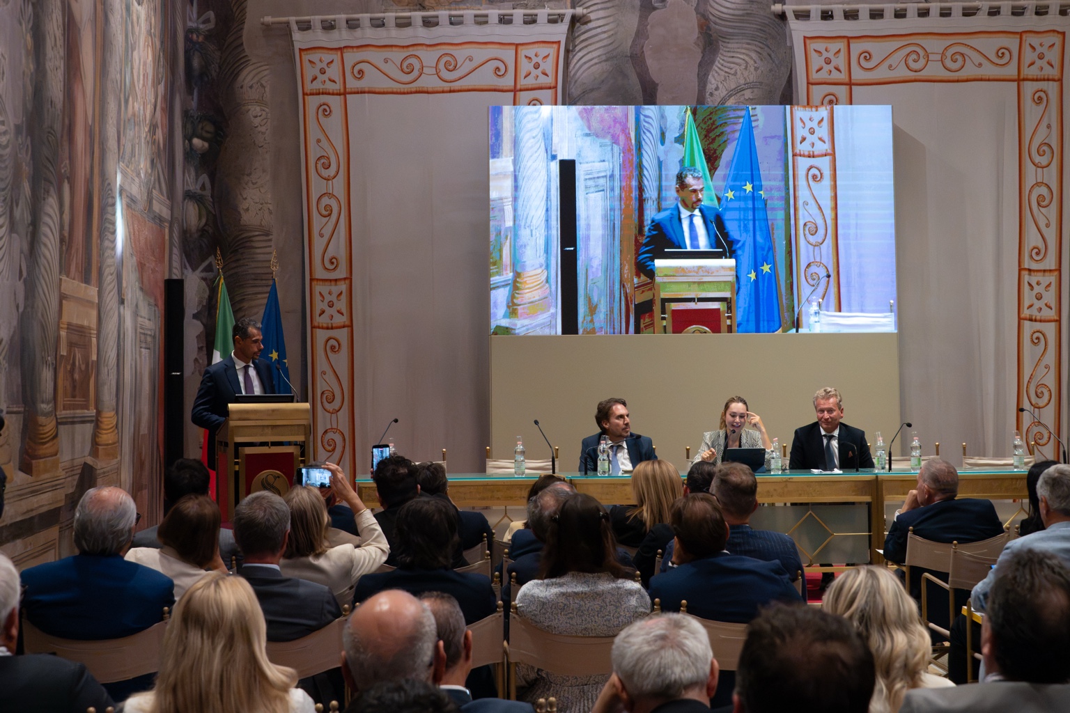 A speaker at the Senate lectern with the panel and audience in Sala Zuccari